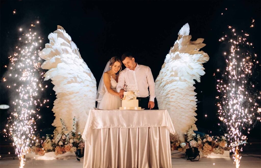 cutting the wedding cake against the backdrop of white wings and a dark night sky