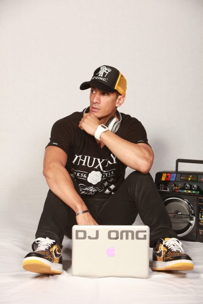 DJ sitting on the ground with a laptop in front of him and a radio at the side of him, with a cap on