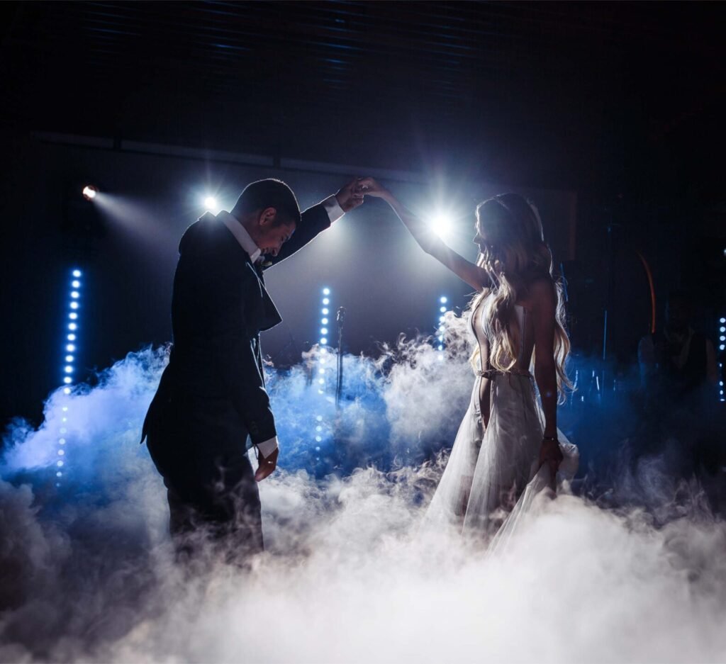 first dance at a wedding. bride and groom form an arch holding hands, they looks like dancing on a clouds with log fog and dry ice at the bottom .